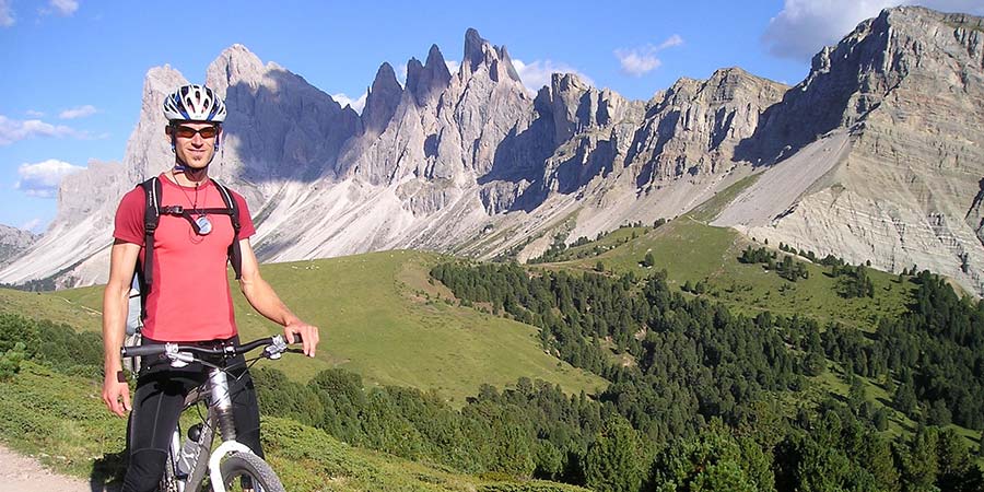 a man in red t-shirt and cycling gear with his bike and a view of the mountains in the background