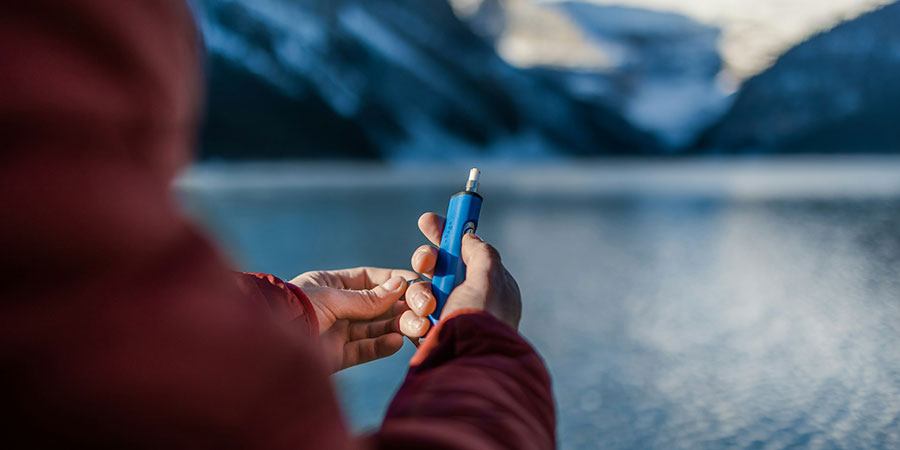 a person in red jacket holding a blue vape device and a view of the mountains and the lake in the background